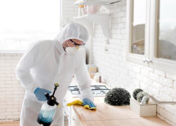 Technicien en combinaison de protection traitant une cuisine contre les cafards et autres nuisibles