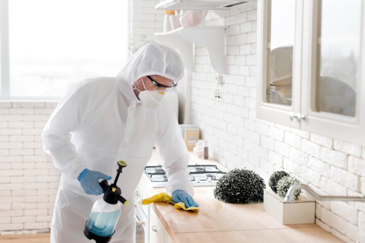 Technicien en combinaison de protection traitant une cuisine contre les cafards et autres nuisibles