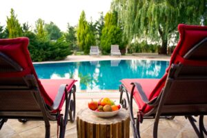 Terrasse de gîte en France avec piscine turquoise, chaises longues rouges et corbeille de fruits