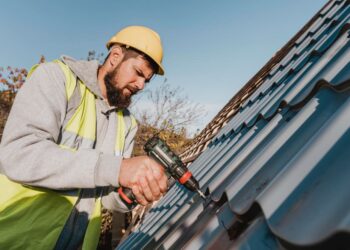 Couvreur professionnel installant des gouttières métalliques bleues sur un toit avec une visseuse électrique