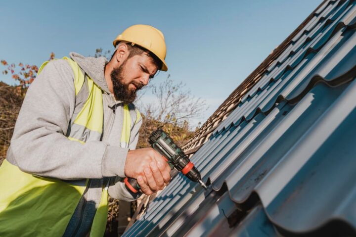 Couvreur professionnel installant des gouttières métalliques bleues sur un toit avec une visseuse électrique
