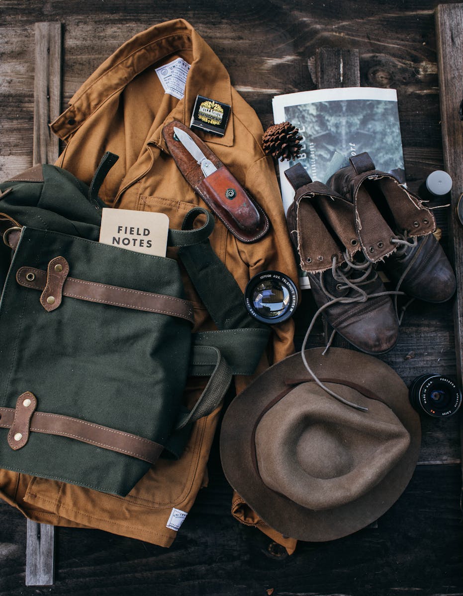 Vue de dessus du costume avec chapeau et bottes à l'ancienne placés sur une surface en bois avec sac à dos et objectif près du journal