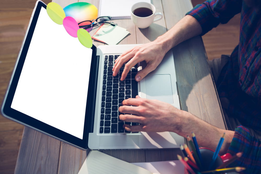 Gros plan sur les mains d'un designer travaillant sur la création d'un site internet sur un ordinateur portable avec des notes colorées